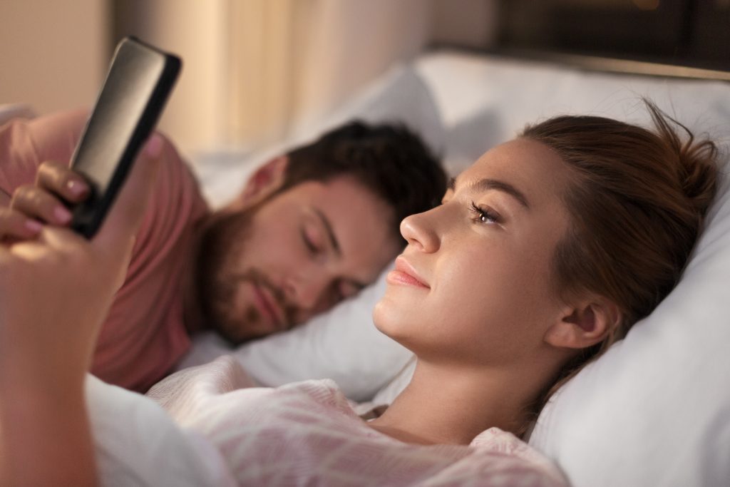 woman using smartphone while boyfriend is sleeping