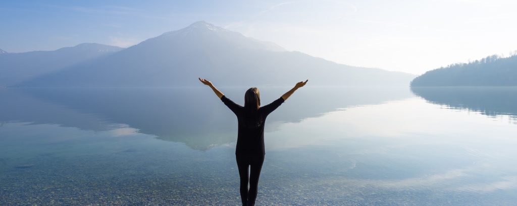 Woman with open arms by the lake on a background of mountains.