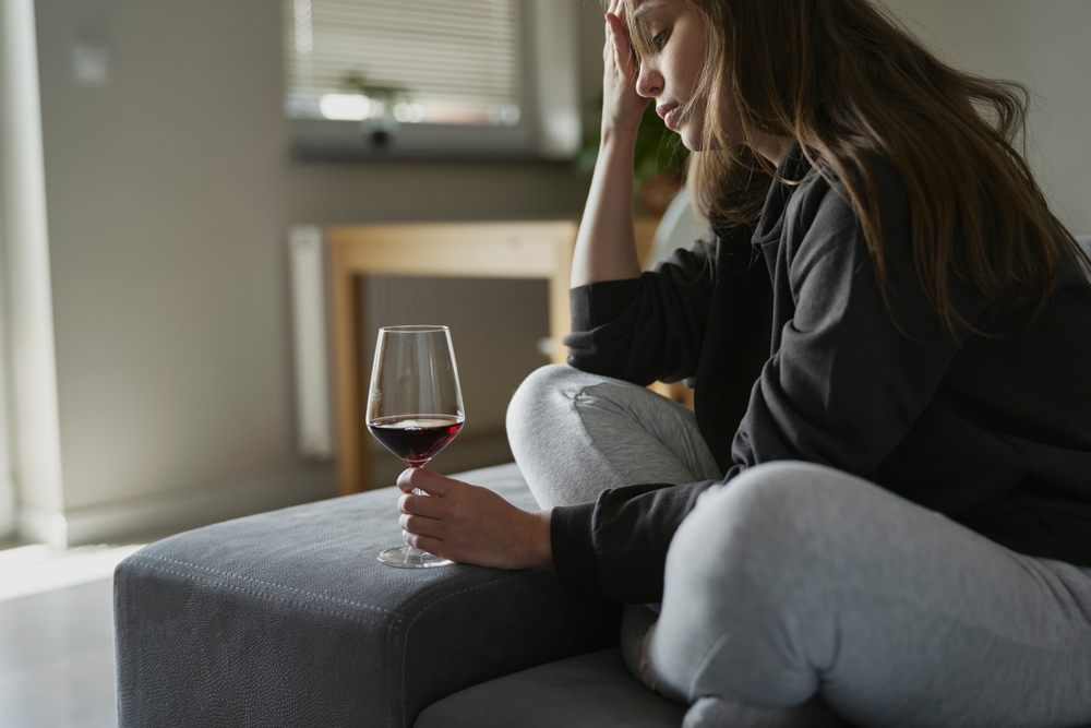 woman sitting on a bed with a glass of wine struggling with her addiction
