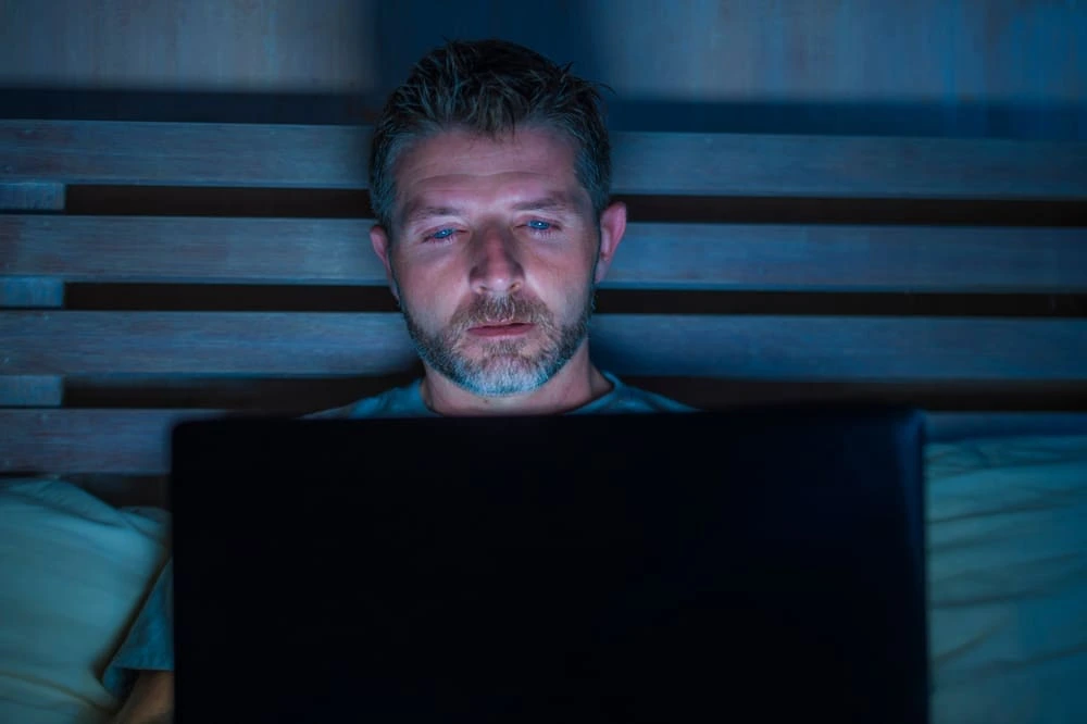 Man in front of a laptop in the dark struggling to turn off from his porn addiction